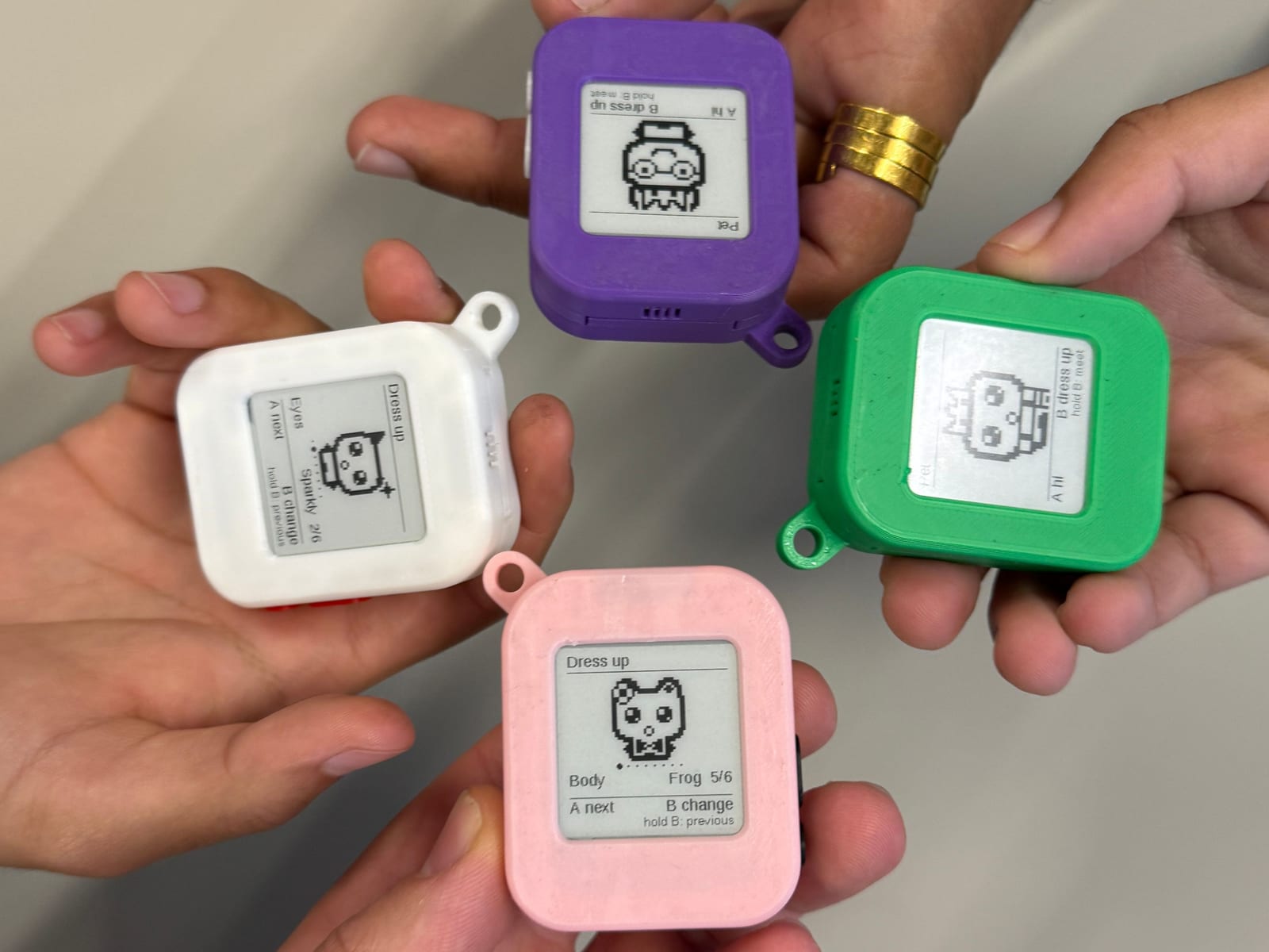 Four unidex in purple, green, white and pink cases, each held in a hand and showing a different Pet